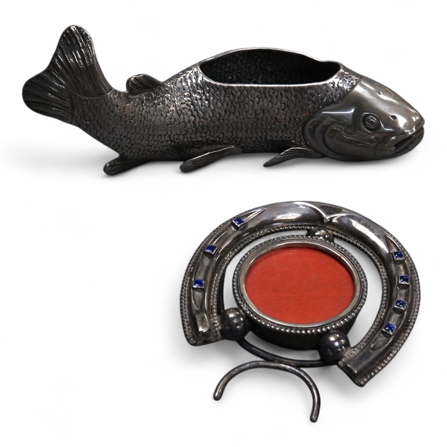 A late Victorian novelty silver and enamelled small photograph frame, modelled as a horseshoe, Birmingham, 1895, height 69mm together with a late 19th century Hanau white metal fish pin cushion(lacking cushion).